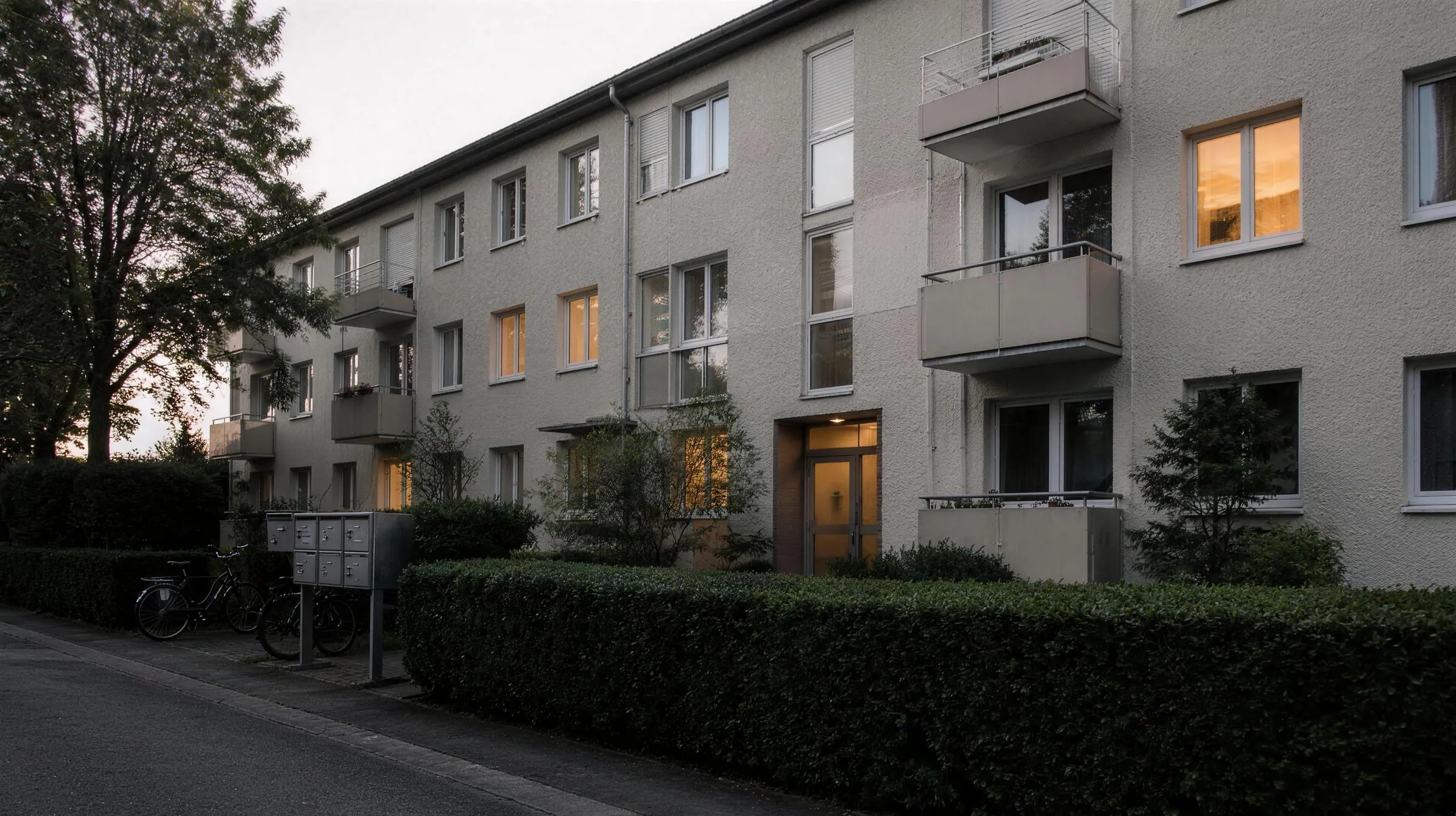 Gepflegtes Mehrfamilienhaus aus den 1960er Jahren mit Balkonen und Vorgarten in der Abenddämmerung (Symbolbild)